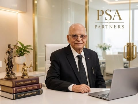 Senior man in business suit sitting at desk with laptop, legal books, and decorative items in modern office with PSA Partners branding